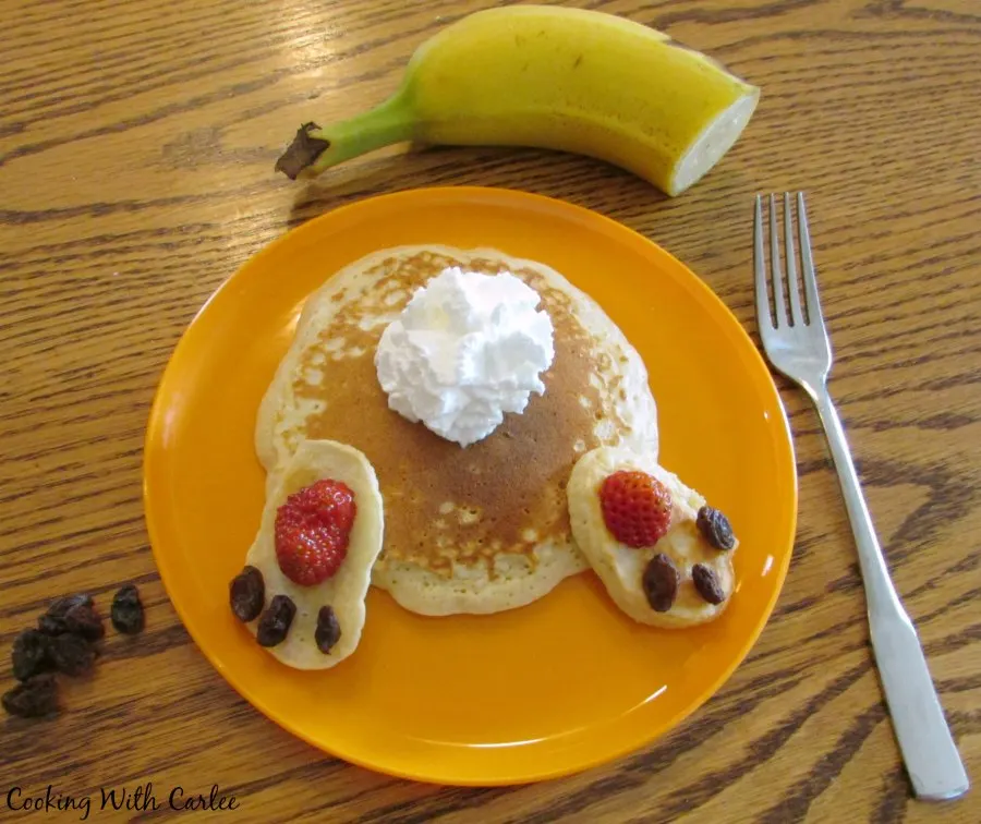 bunny butt pancake on orange plate with banana and additional raisins.