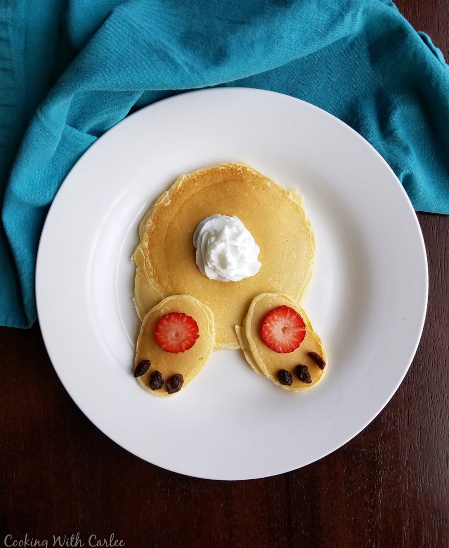 pancakes decorated with strawberry slices, raisins and whipped cream to look like a bunny butt