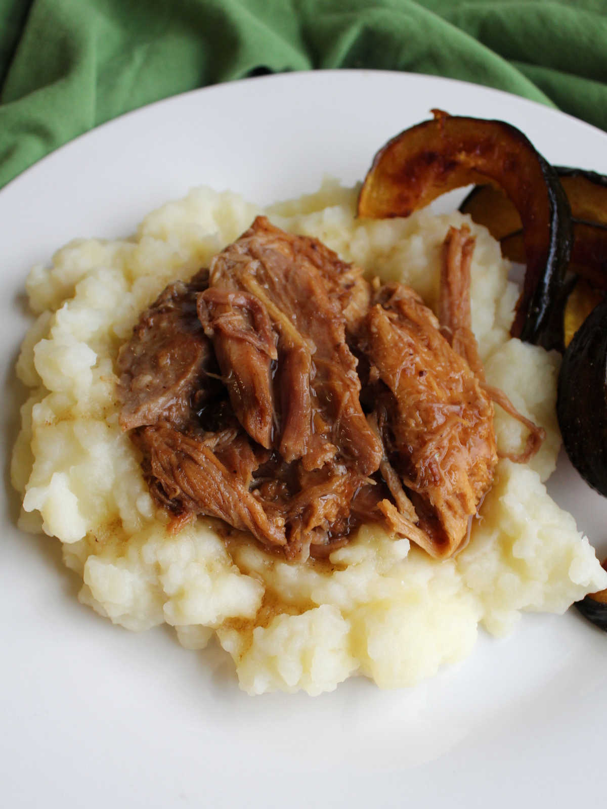 Large chunks of balsamic braised pork on mashed potatoes with roasted acorn squash nearby.
