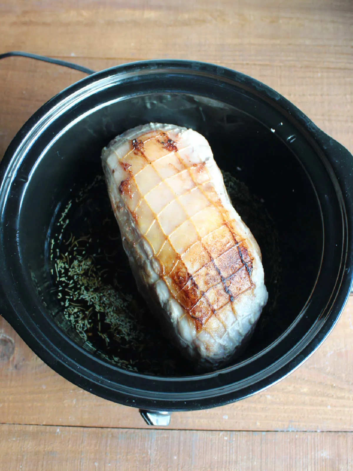 Browned pork shoulder roast in crockpot with balsamic vinegar, honey, and herb mixture ready to cook.