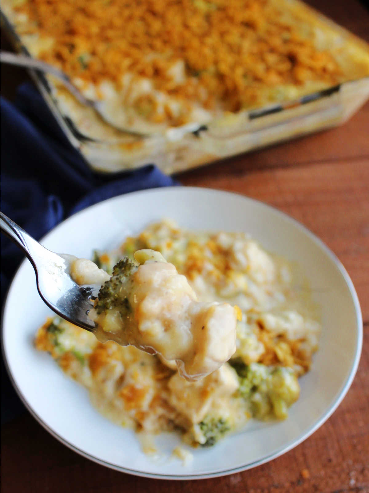 Bite of cheesy chicken broccoli rice casserole on fork showing thick cheese sauce and chunks of chicken and broccoli. 