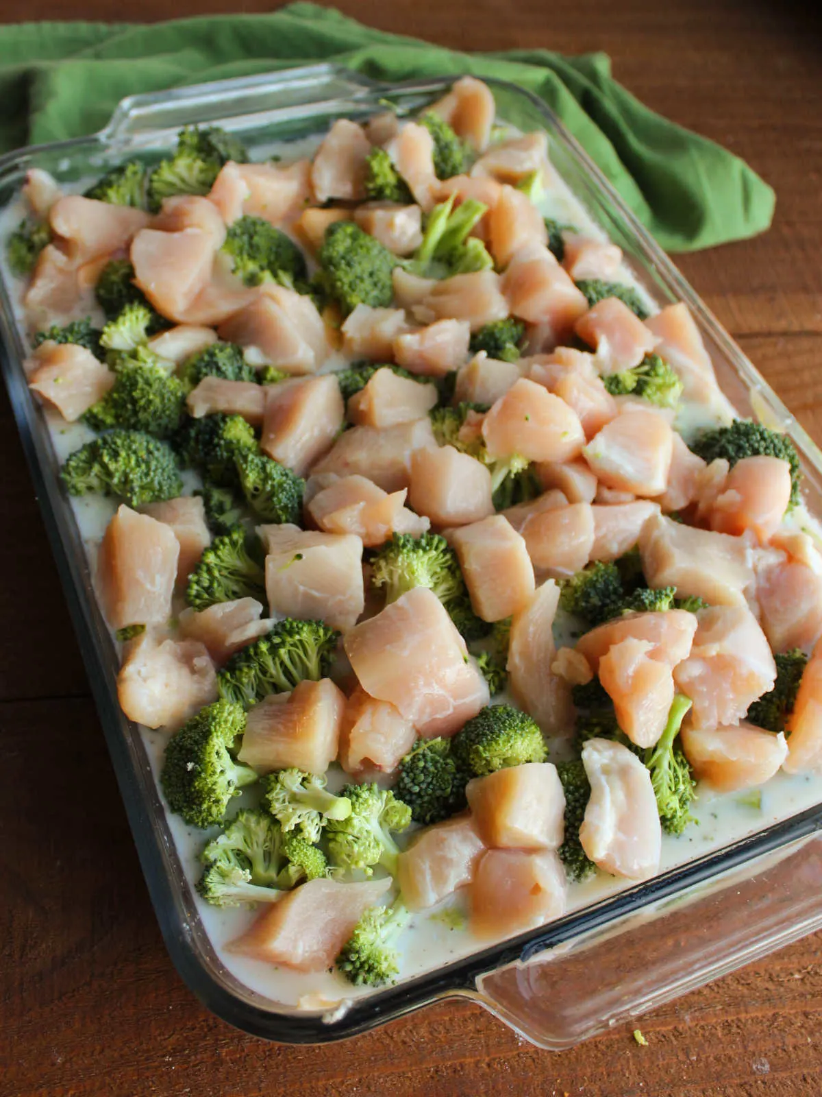 Casserole dish filled with rice and liquid, piled with raw broccoli and chicken, ready to go in the oven.