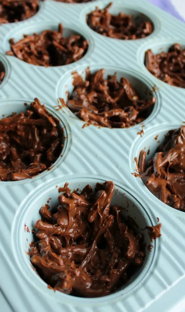 Chocolate and chow mein mixture in cupcake tin being shaped like nests.
