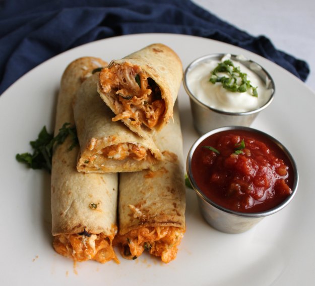 close up look at inside of creamy chicken taquito with bowls of sour cream and salsa for dipping.