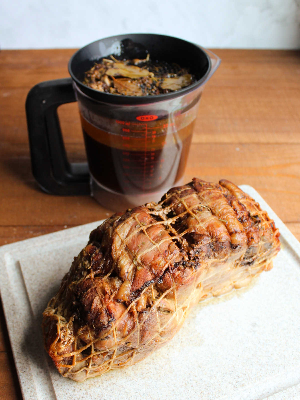 Cooked pork shoulder roast on cutting board with fat separator in the background showing balsamic layer and fat layer.