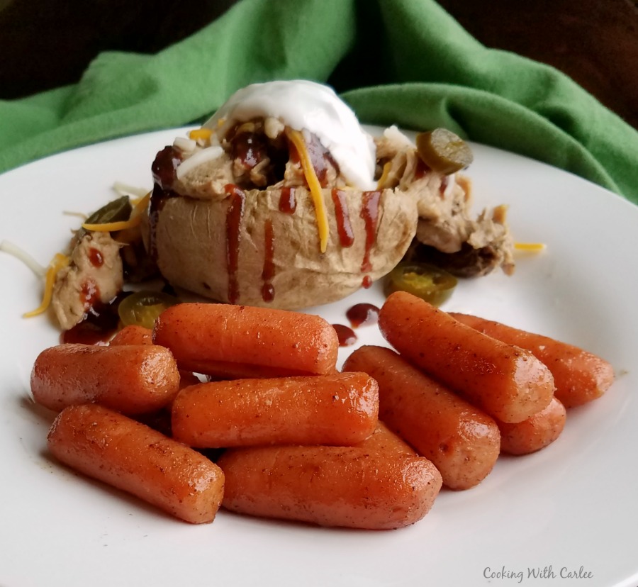 glazed carrots on a plate with pulled pork stuffed baked potato.