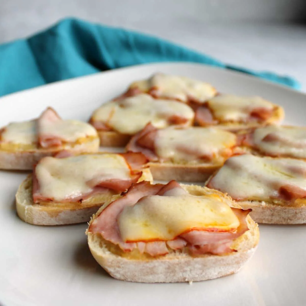 looking across a plate of ham and cheese crostini with melted meunster,