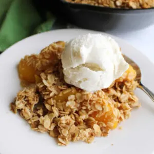 Close up of serving of peach crisp topped with oat topping and a scoop of vanilla ice cream.