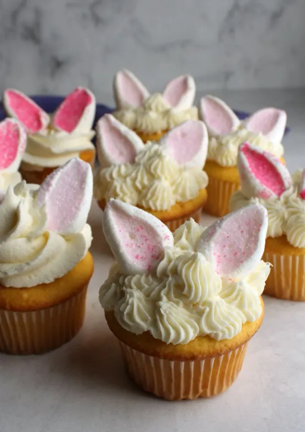 collection of cupcakes with different piping designs for frosting and marshmallow rabbit ears on top, ready for Easter.
