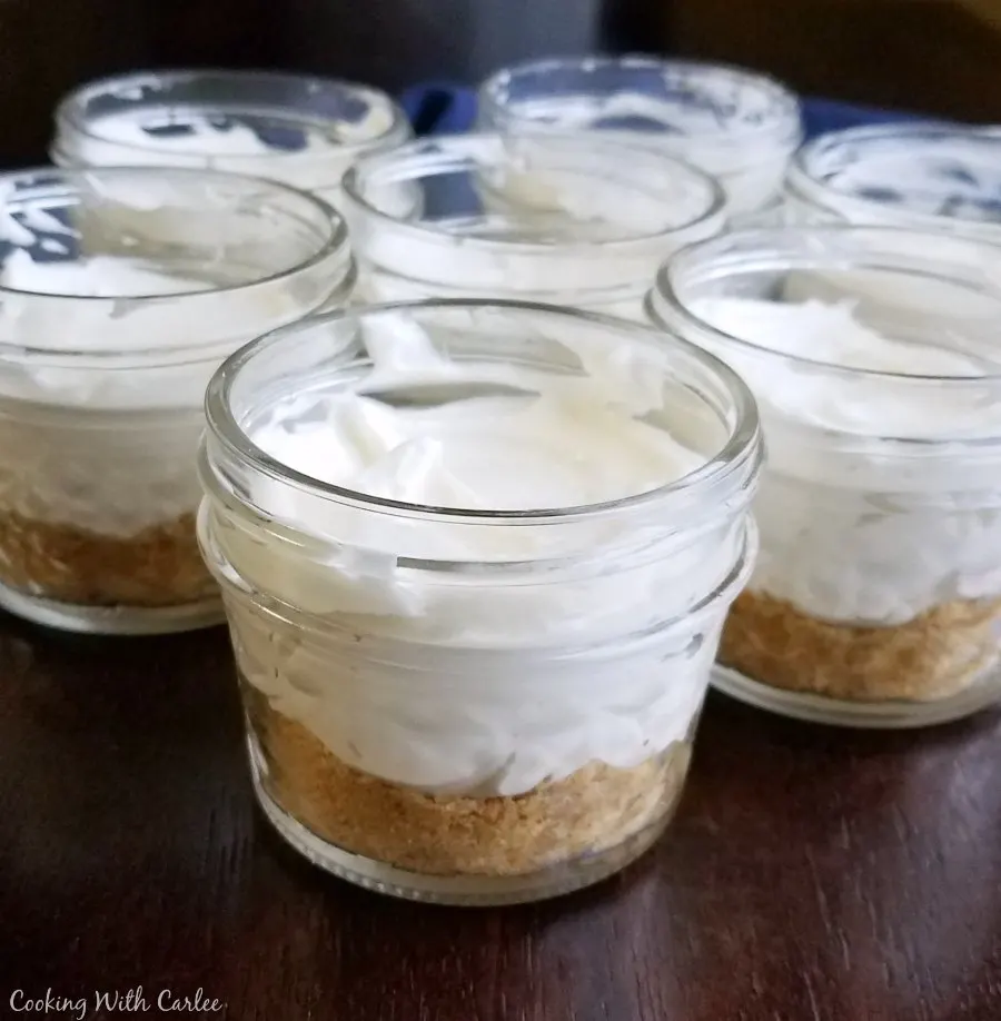 small glass jars with graham cracker crust and no bake lemon cheesecake filling