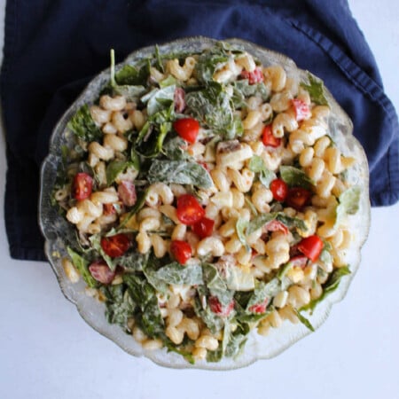 Big glass serving bowl filled with blt pasta salad with corkscrew pasta, baby spinach, chopped tomatoes, bacon, and more in creamy dressing.