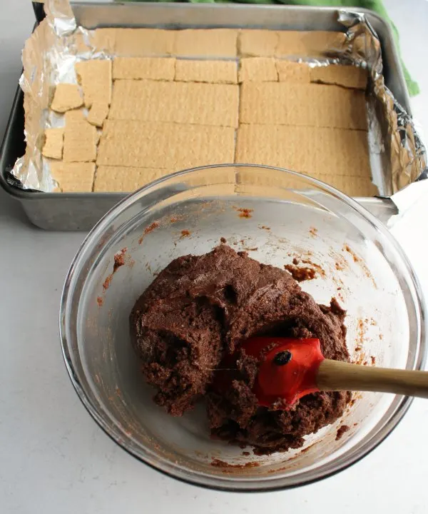 bowl of chocolate cake mix mixture with pan lined with graham crackers in background.