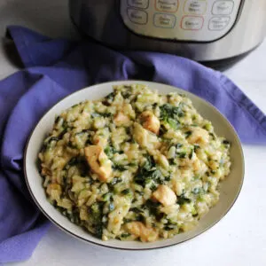 close bowl of risotto with small bits of spinach and chunks of chicken in front of Instant Pot.