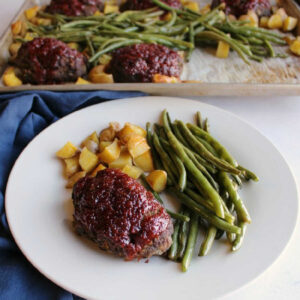 dinner plate loaded with mini meatloaf, green beans and potatoes with pan in background.