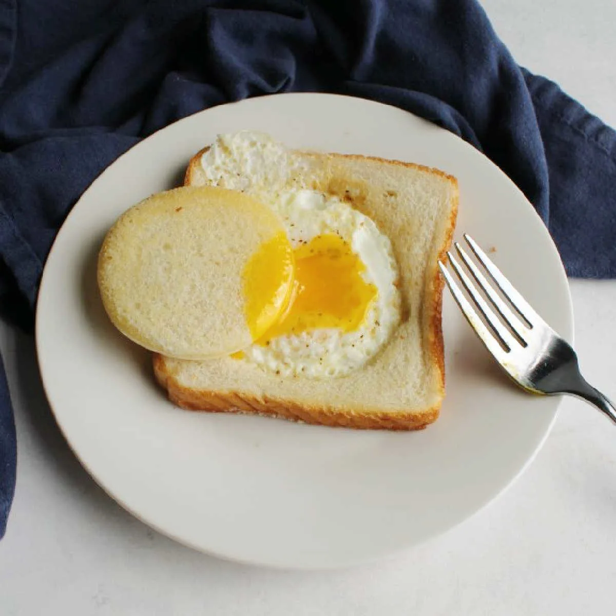 egg in a hole on plate with bread circle dipped in runny yolk.
