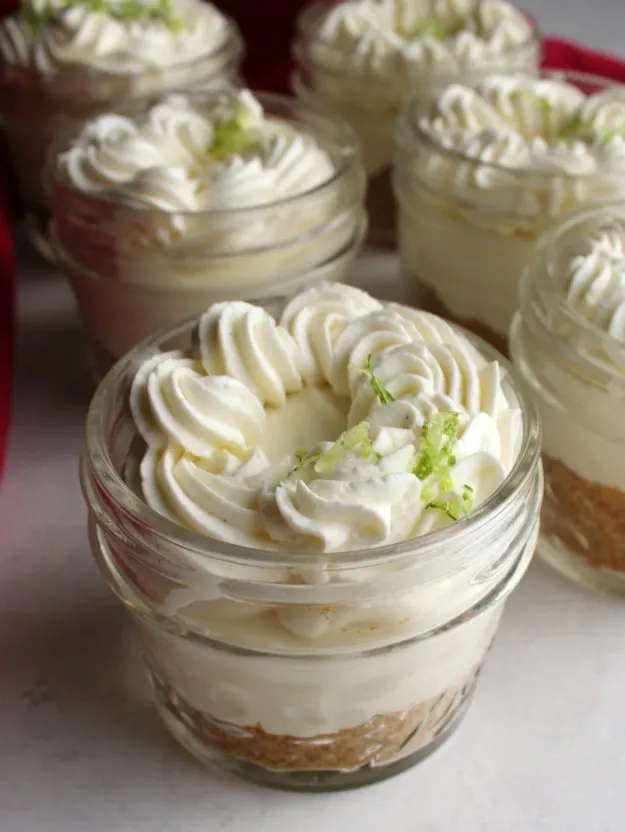 small jars filled with graham cracker crust, key lime cheese cake, and piped cream cheese whipped cream on top