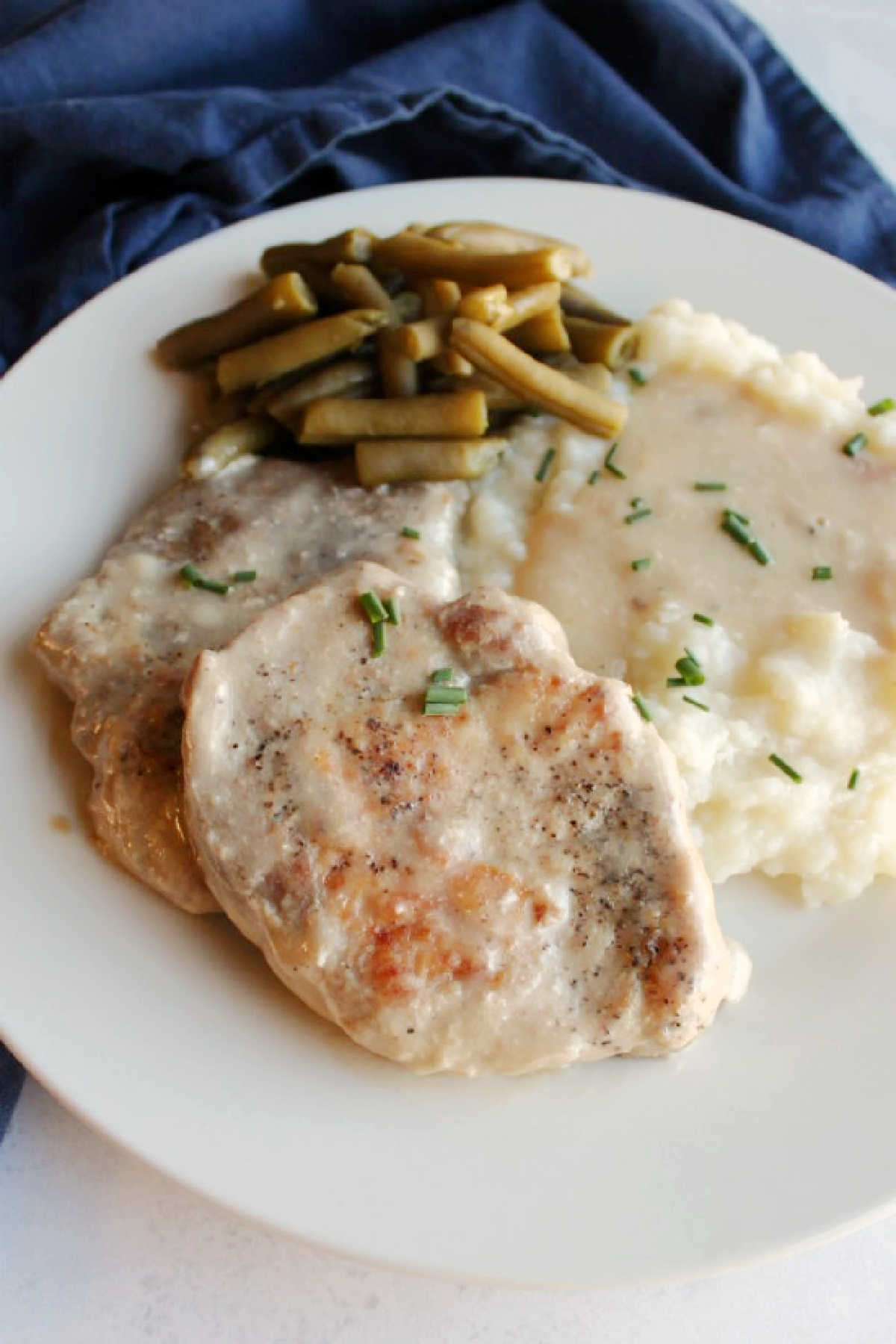 close up of tender pork chops and mushroom soup gravy served with mashed potatoes and green beans.