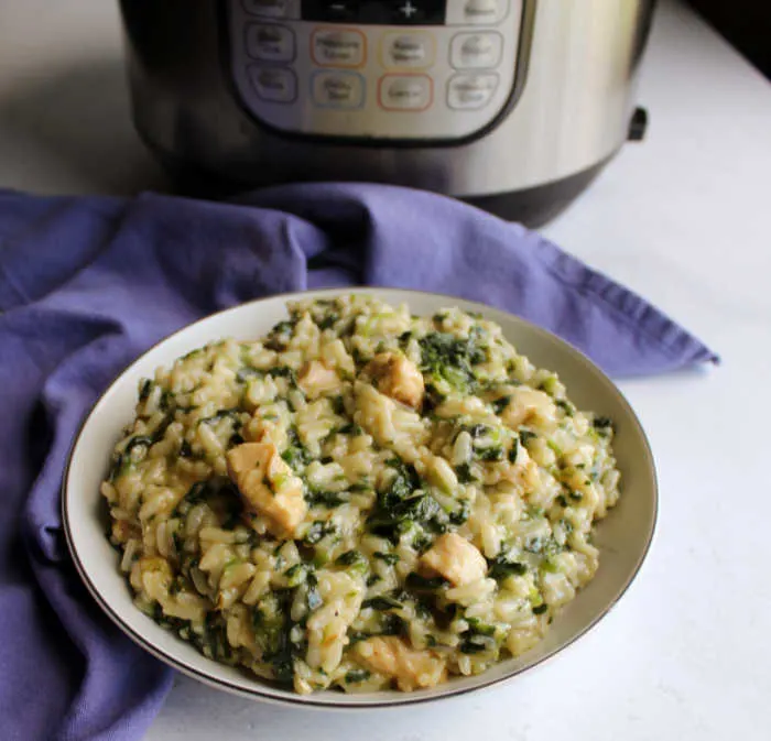 Bowl of spinach and chicken risotto in front of instant pot.