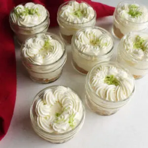 group of small jars filled with key lime cheesecake and topped with whipped cream and lime zest