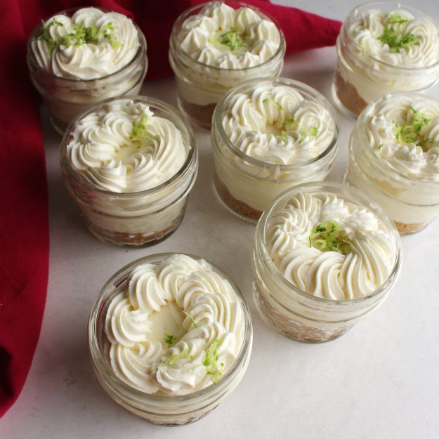 group of small jars filled with key lime cheesecake and topped with whipped cream and lime zest