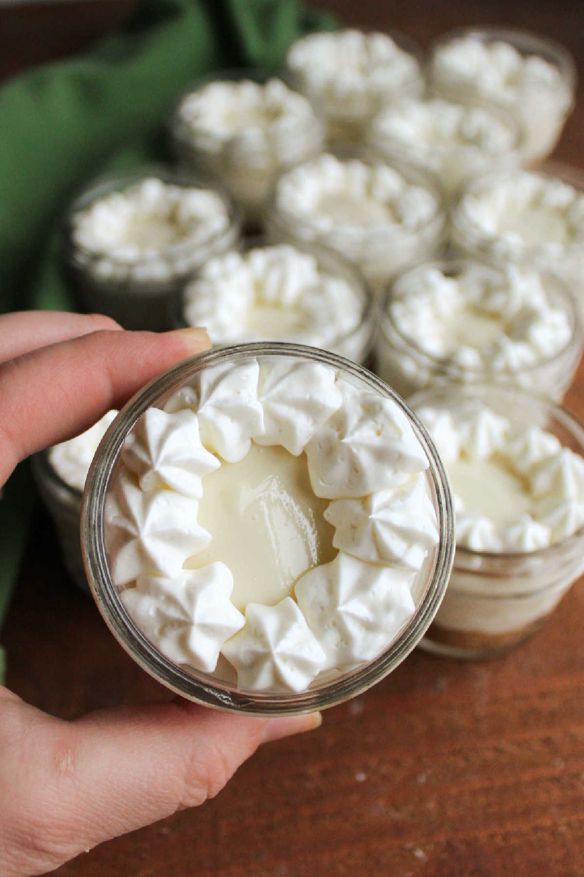 Hand holding jar of no bake key lime cheesecake decorated with a cream cheese whipped cream border, ready to eat. 