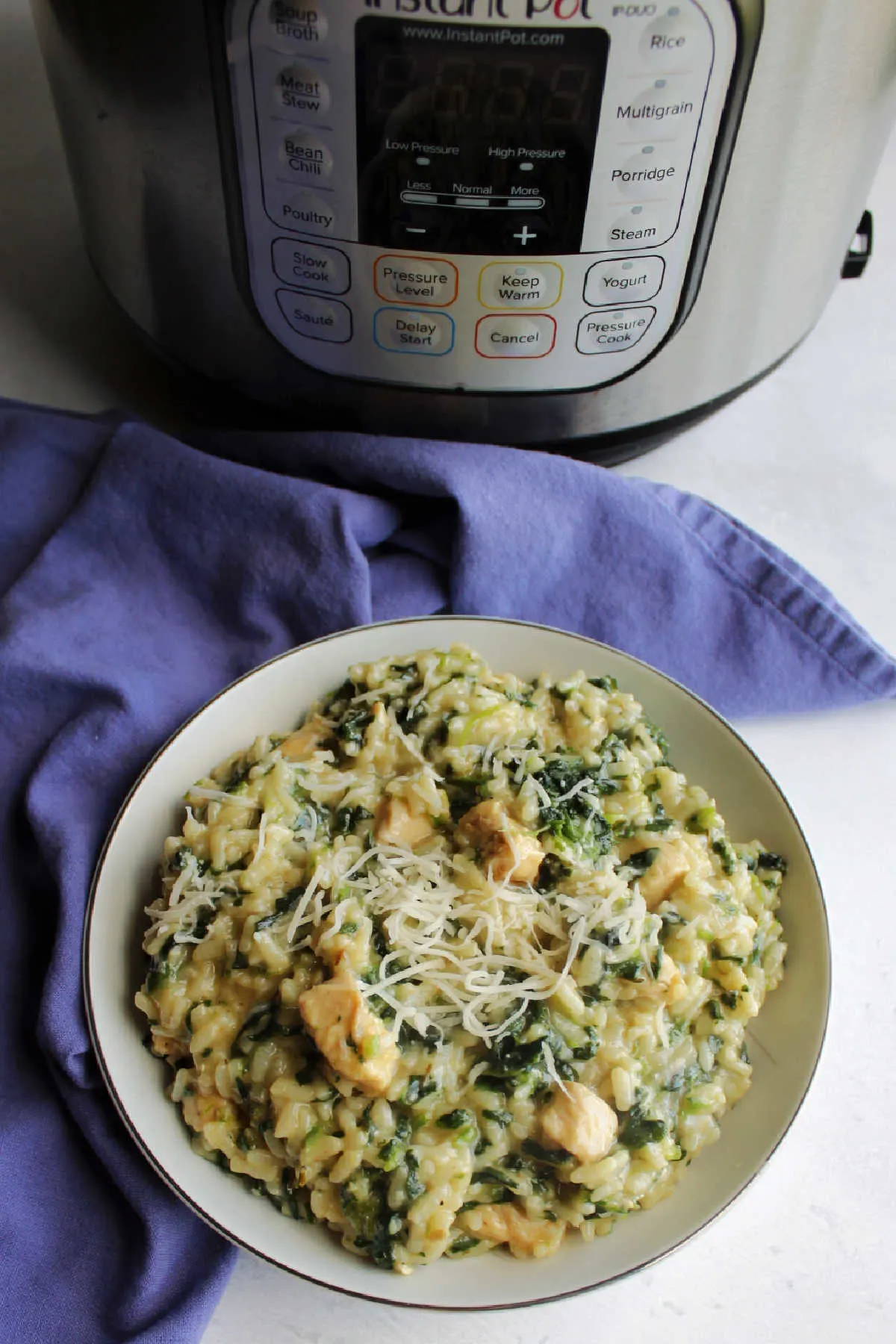 bowl of creamy spinach and chicken risotto topped with shredded Parmesan cheese on top in front of instant pot.
