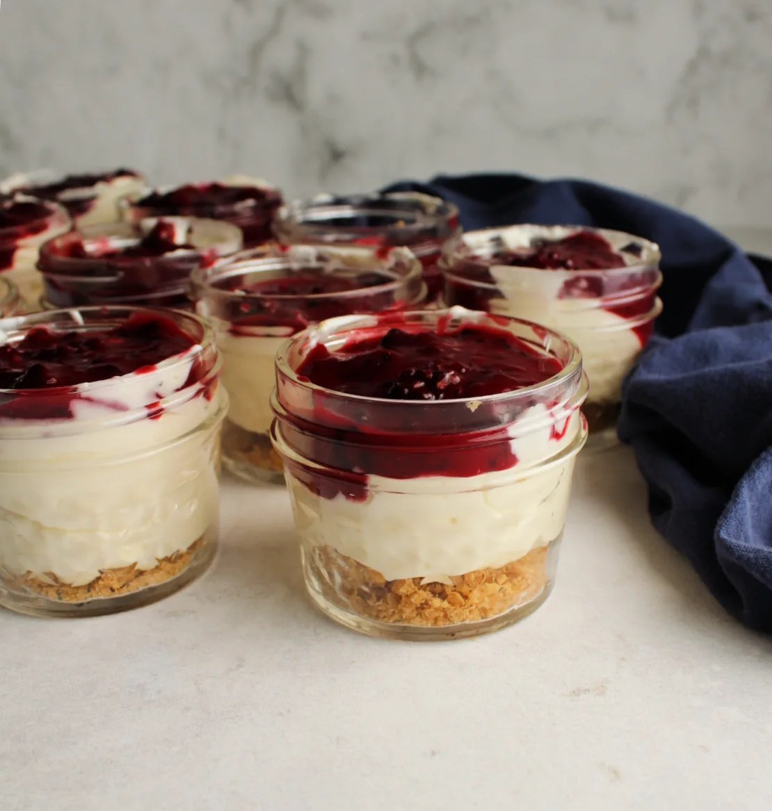 collection of small jars filled with lemon cheesecake mixture and blackberry topping
