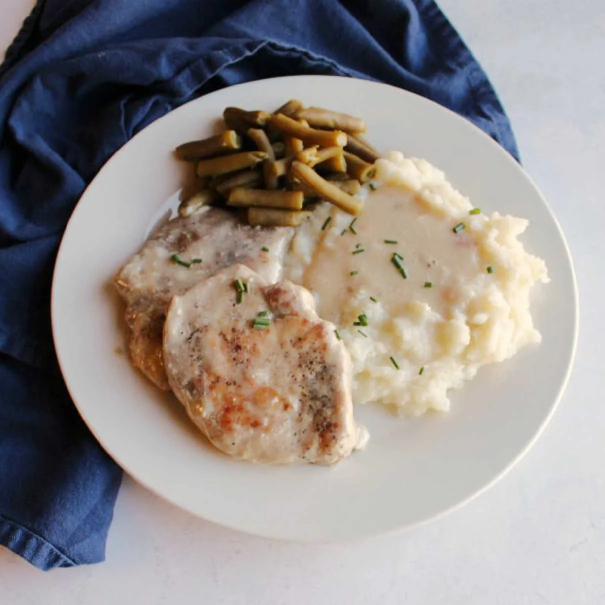 dinner plate filled with pork chops, mashed potatoes, green beans and mushroom soup gravy.