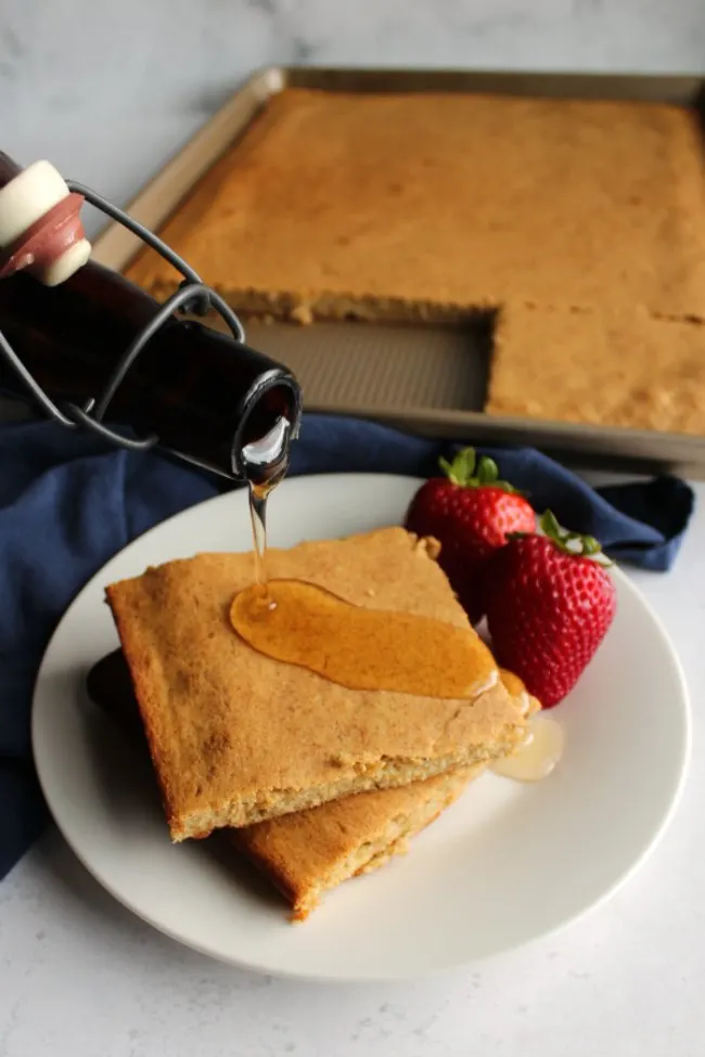 pouring homemade maple syrup over slices of banana sheet pan pancake