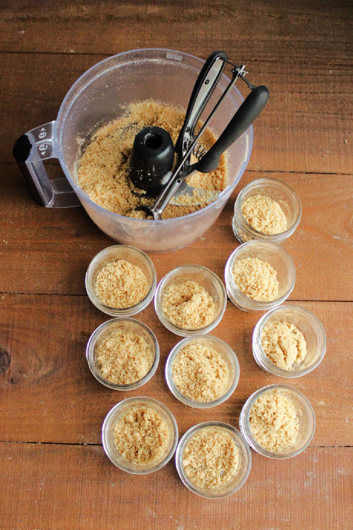 Scooping mixture of graham cracker crumbs, butter and sugar into small jars to make crust for mini cheesecakes.