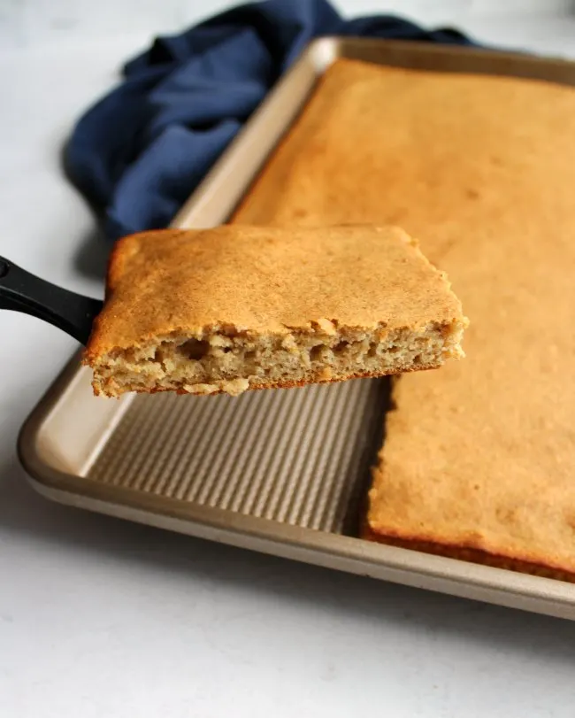 Spatula lifting out square of fluffy banana sheet pan pancake, showing soft texture inside.
