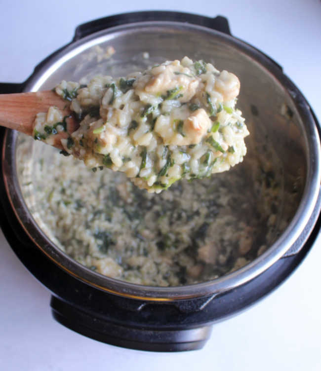 spoonful of steaming hot spinach chicken risotto being lifted out of the pot