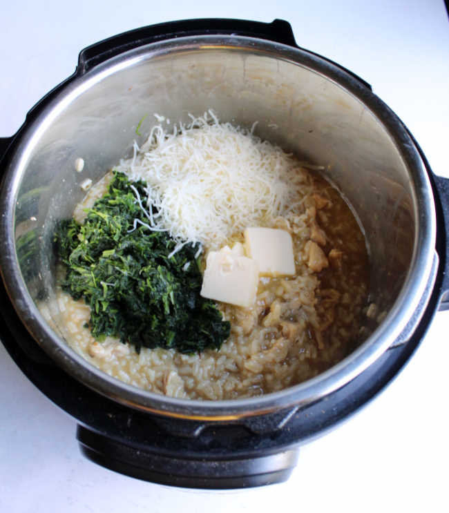 instant pot of freshly made risotto with shredded spinach, cheese and pats of butter on top ready to be stirred in.