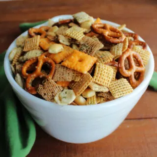 close up bowl of snack mix with pita chips, chex cereal, peanuts, pretzels, cheese crackers all coated in dill and ranch seasoning.