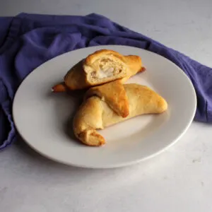 Half of a cream cheese stuffed crescent roll showing the creamy filling perched on top of another golden brown crescent.