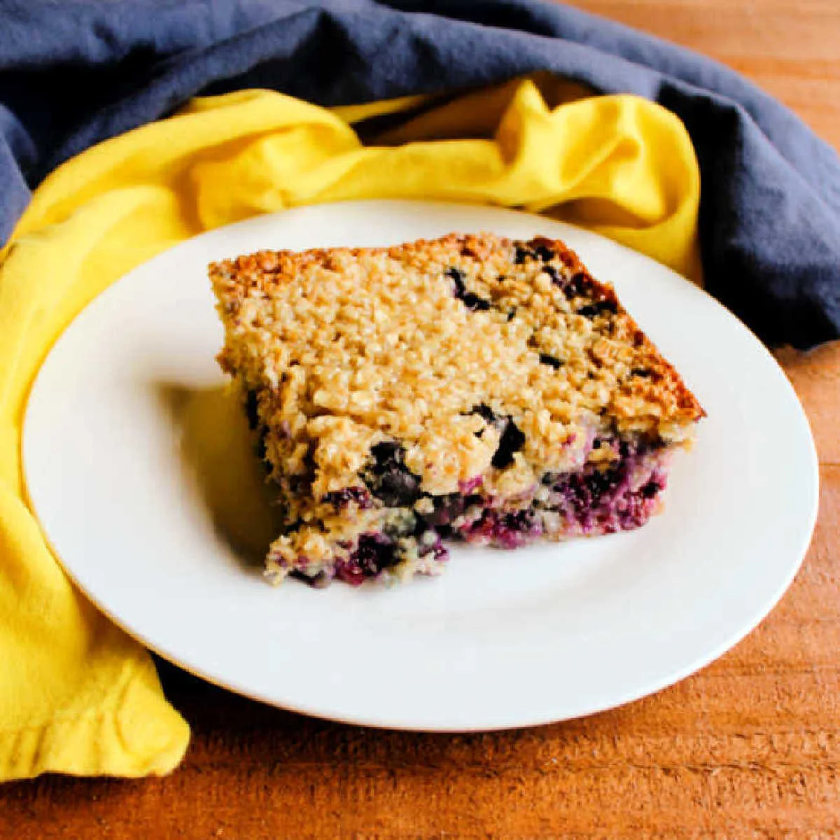 piece of lemon and blueberry baked oatmeal on small plate with blue and yellow napkins nearby