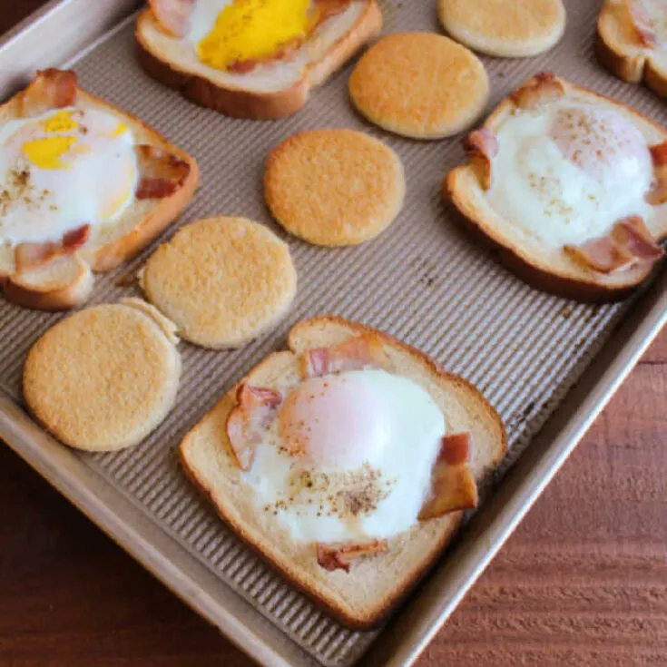 Sheet pan filled with sliced of bread with eggs and bacon cooked in the middle, ready to eat.