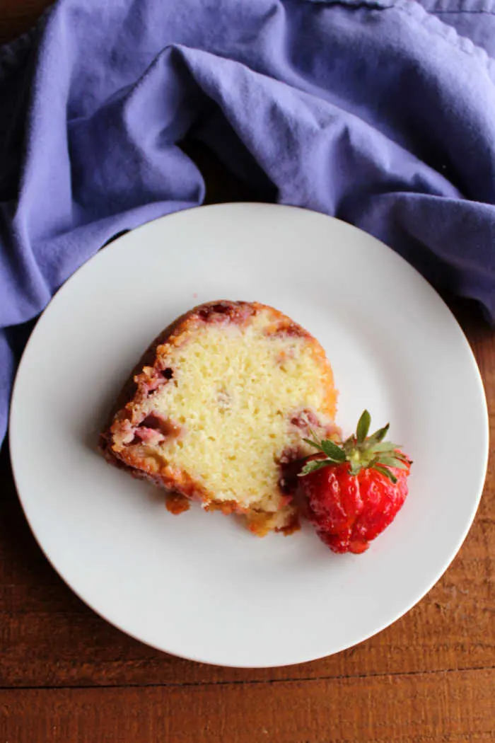 slice of vanilla bundt cake with fresh strawberries baked inside on plate.