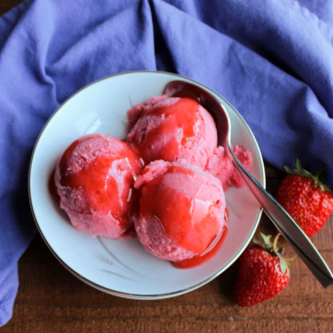 bowl of sherbet with strawberry puree sauce over top.