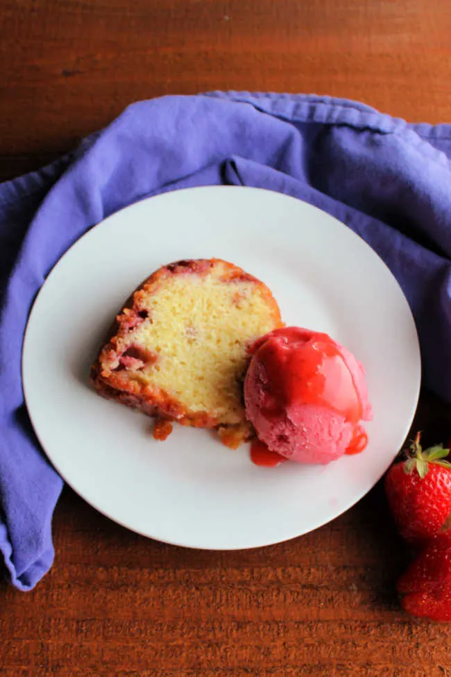 Slice of strawberry sour cream bundt cake served with a scoop of strawberry sherbet and strawberry sauce.
