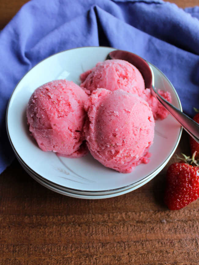 bowl with three scoops of pink strawberry sherbet and spoon