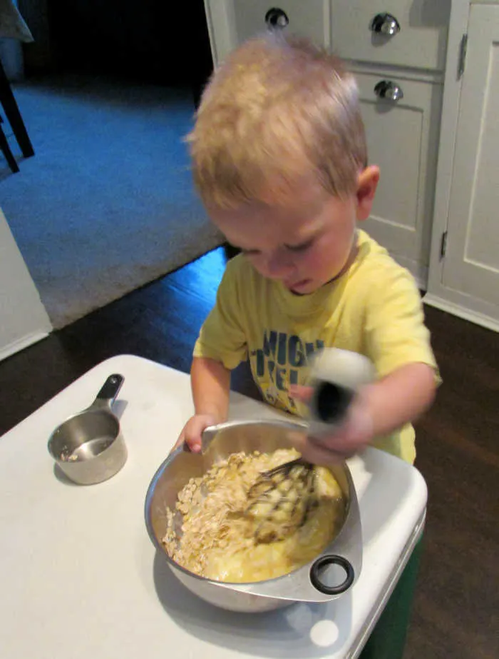 Young kid stirring mixing bowl filled with peach muffin batter.