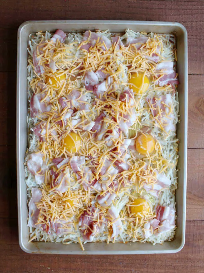 sheet pan filled with hash browns, bacon, eggs and cheese ready to go in oven.