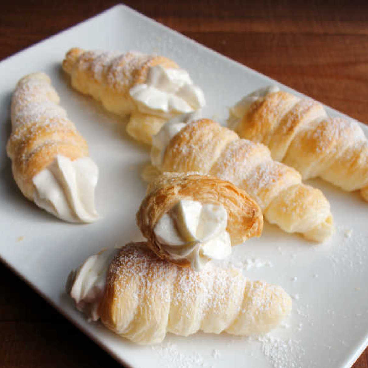 plate of golden cream horns with fluffy filling and dusted with powdered sugar.