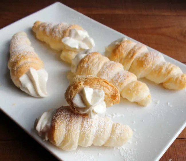 plate of golden cream horns with fluffy filling and dusted with powdered sugar