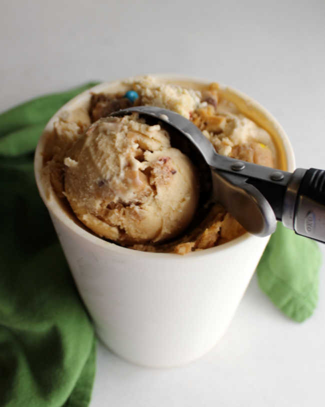 Ice cream scoop dipping out a scoop of monster cookie ice cream with lots of cookie dough bits in a peanut butter ice cream base. 