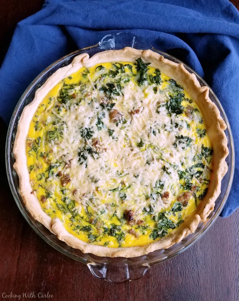 Freshly baked quiche with golden crust, flecks of green kale and plenty of melted cheese on top.