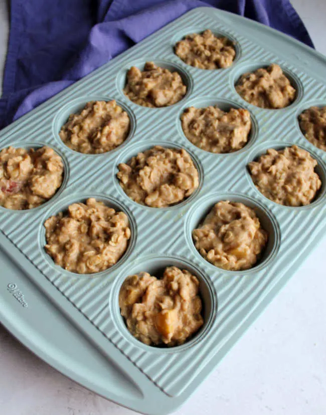 Muffin tin with the wells filled with peach muffin batter, ready to bake. 