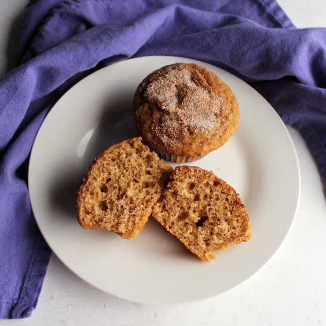 Two cinnamon sugar muffins on a plate, one cut in half showing soft interior.