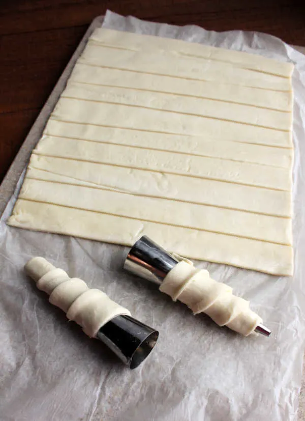 strips of puff pastry with two rolled around metal cone shaped molds